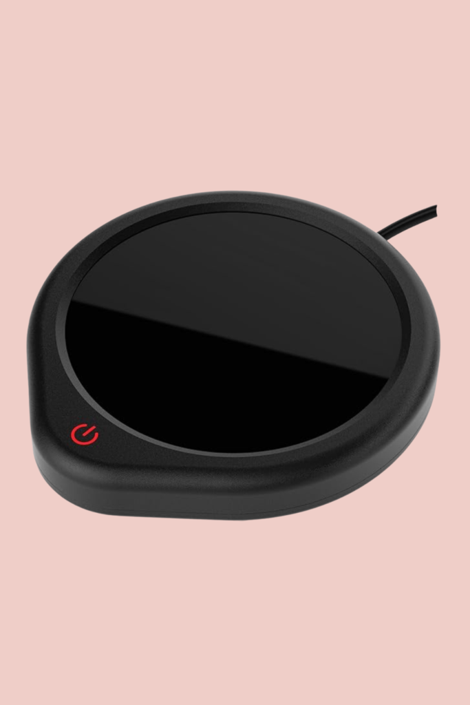 Black electric mug warmer on a pink background, ideal for keeping coffee or tea hot while reading