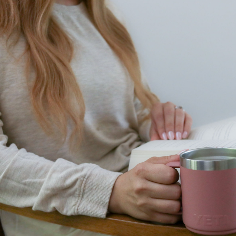 Woman reading a book with coffee mug, learning how to annotate and remember more from her reading.