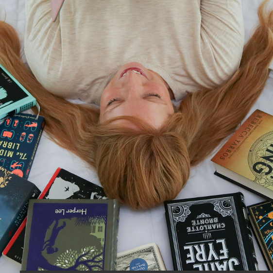 Woman surrounded by books, holding an e-reader, exploring book recommendations and organizing her TBR list.