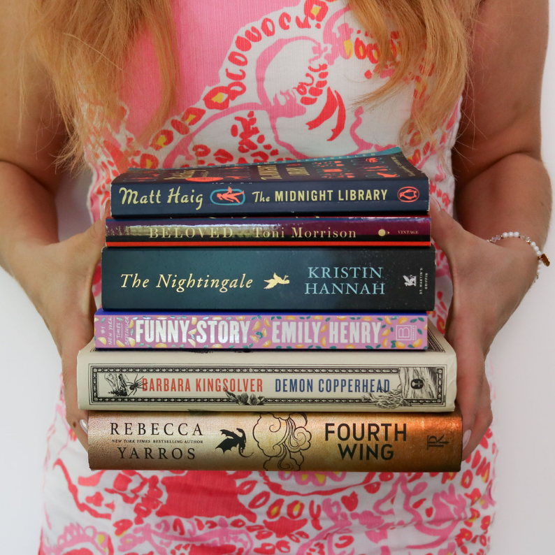 Woman holding stack of popular books, including Fourth Wing and The Midnight Library, featuring trending BookTok favorites.
