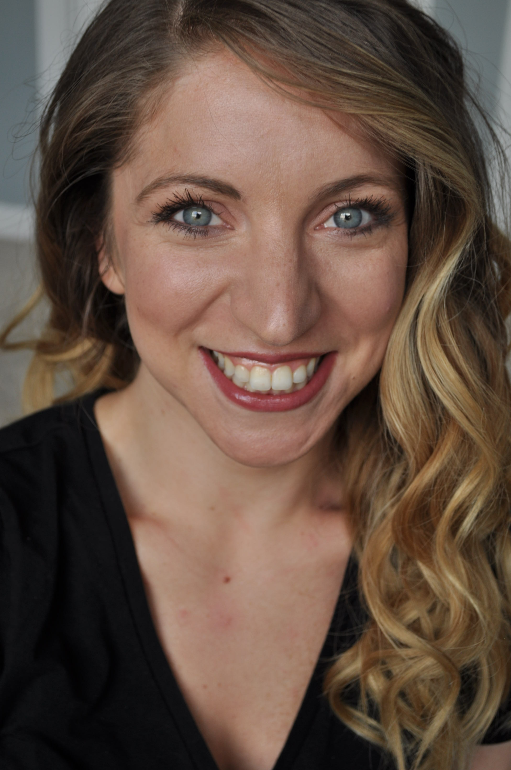 Close-up smiling headshot of woman with curled blonde hair and soft makeup