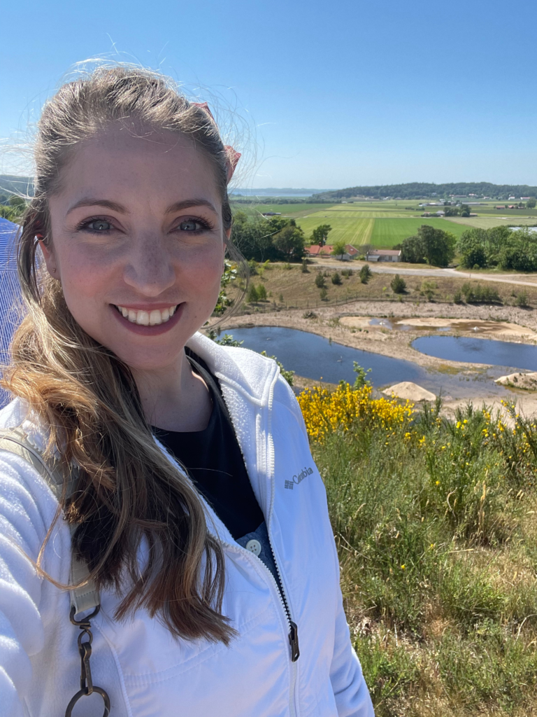 Woman smiling outdoors on a scenic hike, wearing a white Columbia fleece