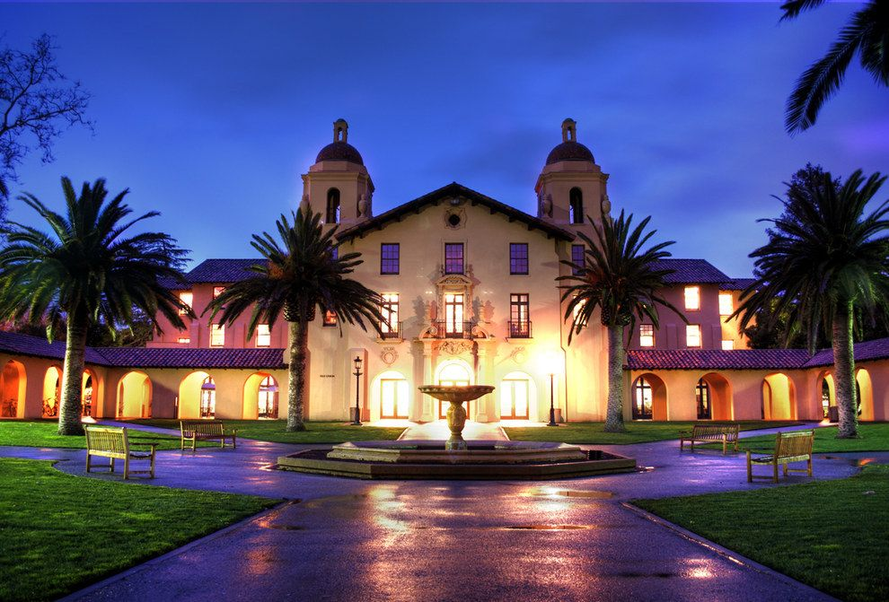 Stanford University building illuminated at night with fountain and palm trees, highlighting the atmospheric campus setting in Deep End by Ali Hazelwood.